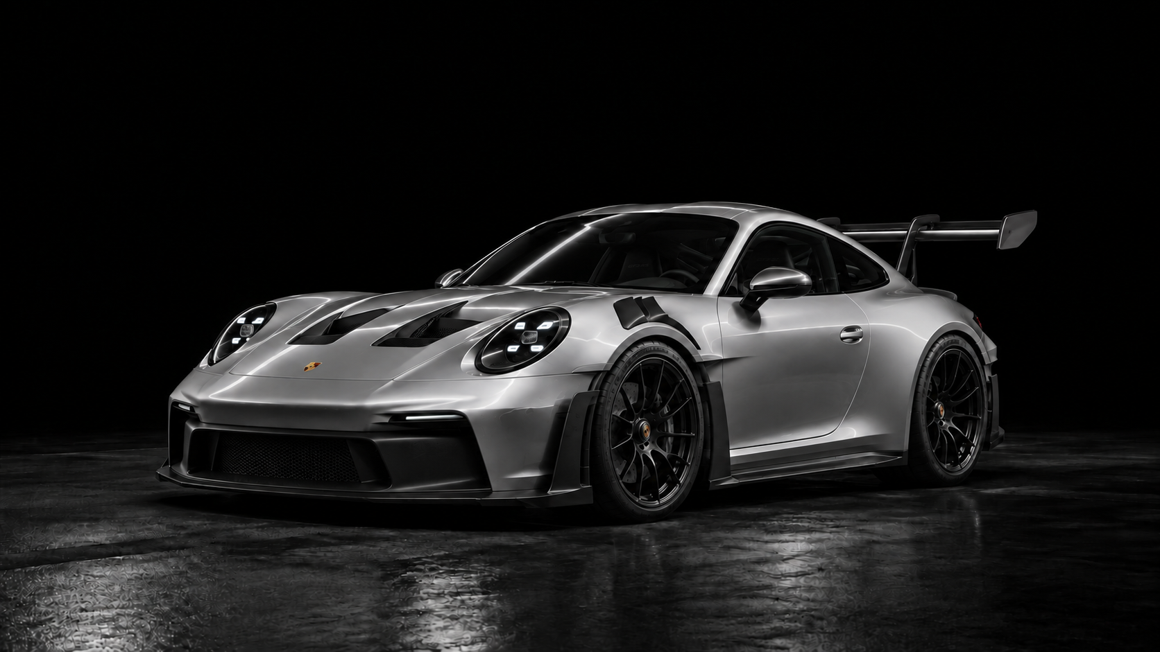 Silver Porsche 911 GT3 RS with a tall rear wing and sculpted aero details, illuminated against a black background